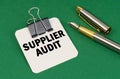 On a green surface, a pen and a sheet of paper with the inscription - Supplier Audit