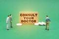 On the green surface are pills, miniature figures of people and a sign with the inscription - Consult your doctor Royalty Free Stock Photo