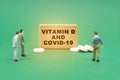 On the green surface are pills, miniature figures of people and a sign with the inscription - Vitamin D and covid-19