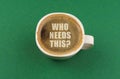 On a green surface there is a white cup with coffee, on the coffee foam there is an inscription - Who Needs This