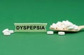 On a green surface, a wooden spoon with pills and a sign with the inscription - DYSPEPSIA