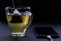 Green tea in a pyramid tea bag is brewed in hot water in a transparent cup next to a charging smartphone. The concept of Royalty Free Stock Photo