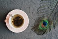 Green tea in a small pink cup and decorative peacock feather on concrete table