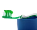 Green toothbrush with paste lying on blue plastic cup isolated over white background Royalty Free Stock Photo