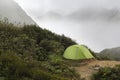 Green tourist tent on a background of mountain peaks in the fog. Royalty Free Stock Photo