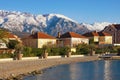 Green town at foot of snowy mountains. Montenegro, view of embankment of Tivat city and Lovcen mountain on sunny winter day