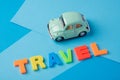 Green toy car and inscription plastic travel letters on a blue b