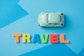 Green toy car and inscription plastic travel letters on a blue b