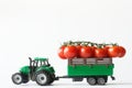 Green toy tractor is transporting a branch of fresh red cherry tomatoes in a trailer. White background. Harvest and delivery Royalty Free Stock Photo