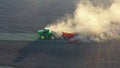 Green tractor cultivating ground and seeding a dry field.