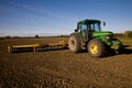 Green tractor with harrow on tilled field