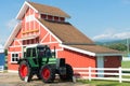 Green Tractor and Red Barn with blue sky and white fence. Royalty Free Stock Photo