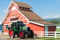 Green Tractor and Red Barn with blue sky and white fence.
