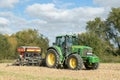 A green tractor with a seed drill in a stubble field