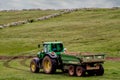 Green tractor with trailer in a green field. Agriculture industry. Heavy machinery in action in rural area Royalty Free Stock Photo