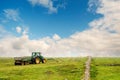 Green tractor with trailer in a green field on a hill. Agriculture industry. Heavy machinery in action in rural area. Beautiful Royalty Free Stock Photo
