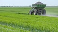 A green tractor is working in a field of wheat. The wheat is growing tall and green. The sky is blue with white clouds Royalty Free Stock Photo