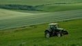 A green tractor is working in a field of wheat. The wheat is growing tall and green. The sky is blue with white clouds Royalty Free Stock Photo