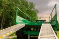 Green trailer in a field with ramp down by a forest. Concept heavy machinery delivery