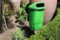 Green Outdoor Trash Can and Some Plants around It