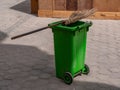 Green trash can and street cleaning broom.