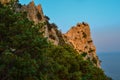 green trees and bushes, sharp rocks, cliff against the backdrop of blue sea in red orange light of setting sun. Crimea landscape. Royalty Free Stock Photo