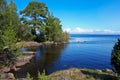 Green trees and grass on shore of the blue Lake Ladoga. Bay in the rocks on a clear summer sunny day. Blue sky with white Royalty Free Stock Photo