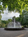 green trees in the park, a fountain, under the crown of a tree, clouds against a bright sky, for postcards, business cards