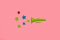 green trumpet from which colorful stars are heard, creative art design on pink background, new information