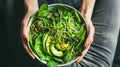 Green vegan breakfast meal in bowl with spinach, arugula, avocado, seeds, and sprouts Woman in leggings holding plate with hands