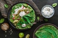 Green vegan crepes with spinach or pancakes with cottage cheese, pomegranate, nuts and spinach leaves on black plate over dark