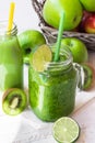 Green vegetable smoothie in jar mug, bottle with fresh fruit juice, apples, citrus, kiwi, on wood table outdoors