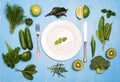 Green vegetables fruit and herbs around white plate and silverware on wooden blue background. Detox and diet concept. Royalty Free Stock Photo