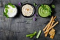 Green vegetables raw snack board with various dips. Yogurt sauce or labneh, hummus, herb hummus or pesto with crackers, grissini b