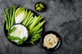 Green vegetables snack board with various dips. Yogurt sauce or labneh, hummus, herb hummus or pesto with fresh vegetables.