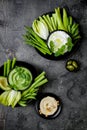 Green vegetables snack board with various dips. Yogurt sauce or labneh, hummus, herb hummus or pesto with fresh vegetables.
