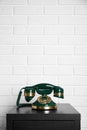 Green vintage corded phone on small black table near white brick wall. Space for text Royalty Free Stock Photo