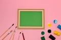 green vintage school blackboard as copy space on pink background, next to it are brushes and paint Royalty Free Stock Photo