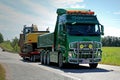 Green Volvo FH Hauls Tracked Excavator along Highway at Summer