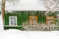 The green wall of Russian old-fashion wooden house with wooden windows, roof covered by snow and huge icicles on its edge with