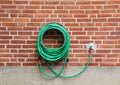 Green water hose hanging red brick wall Royalty Free Stock Photo