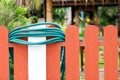 Green watering hose is rolled up over the red fence for safety and tidy and easy to spot as it is stored up high. Red fence