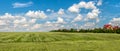 A green wheat field on the hills, a village on the horizon and a blue cloudy sky