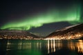 a green and white aurora bore over a lake and a town at night with lights on the mountains in the background and a city in the Royalty Free Stock Photo