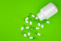 Green and white pill capsules with white pill bottle over green background, medical treatment, pharmaceutical or medication Royalty Free Stock Photo