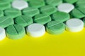 Green and white pills scattered on yellow background. Helth and medical concept.