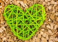 Green wicker heart symbol of love of family loyalty against the background of a piece of wood chips