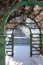 Green wooden arch pergola with a lantern in Kadriorg park covered with dry branches on a sunny day. Stair steps on the