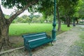 Green wooden bench at sidewalk in public park to sit under the trees for relaxation Royalty Free Stock Photo