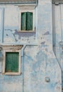 Green wooden windows with peeling paint on an old, blue wall of the house. Royalty Free Stock Photo